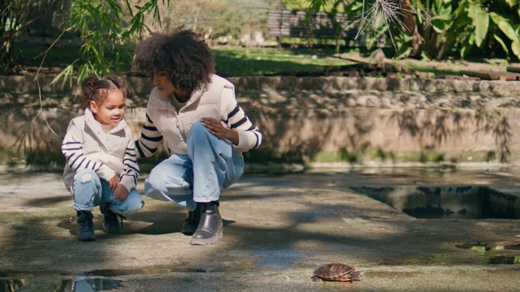 Woman girl watching reptile in sunny park. African family enjoying wildlife.