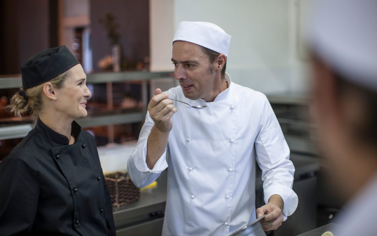 Chefs chatting and tasting food in kitchen